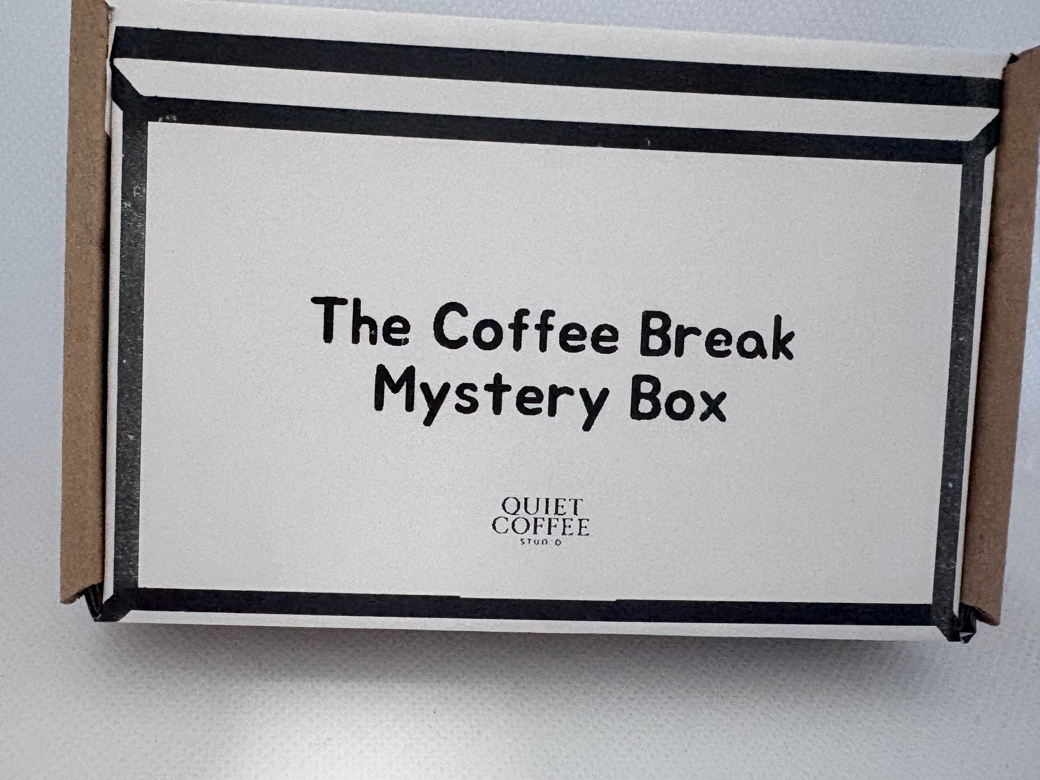 A white cardboard box labeled 'The Coffee Break Mystery Box' with 'Quiet Coffee Store' printed below, photographed on a light gray surface.