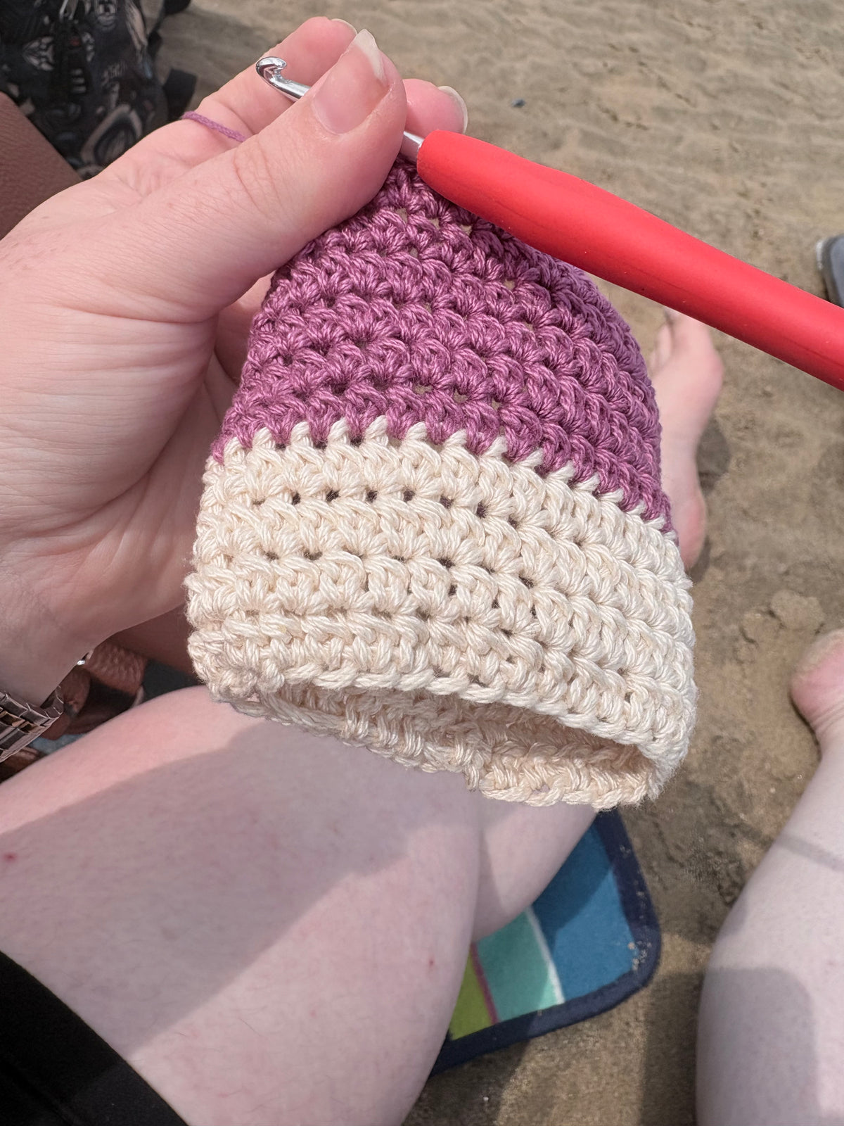 Handmade crochet cup sleeve in lavender purple and cream stripe, being crocheted on the beach
