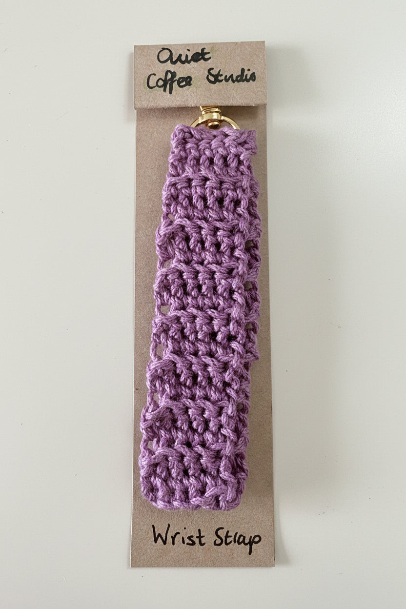 A lavender purple crocheted wrist strap with a gold metal clasp, attached to a brown cardboard display card labeled 'Quiet Coffee Studio' and 'Wrist Strap'.